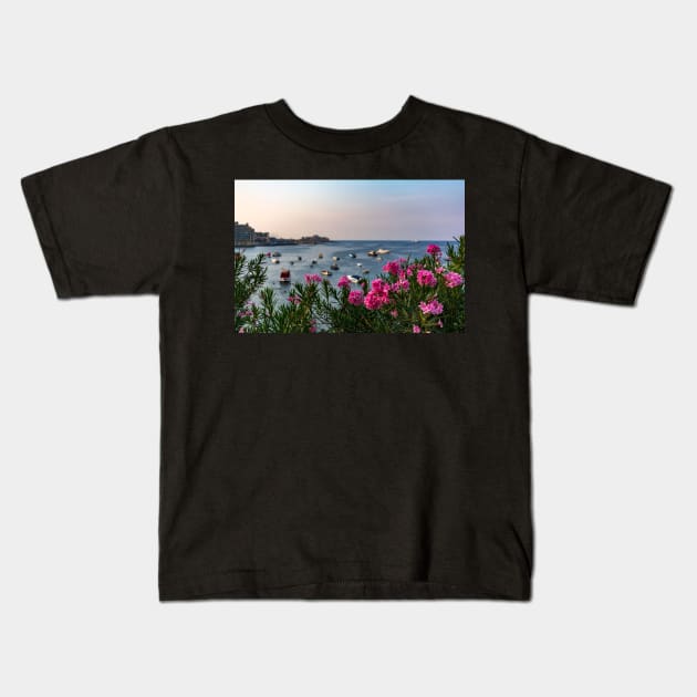 Pink Nerium oleander flowers with Malta Bay in the background Kids T-Shirt by lena-maximova